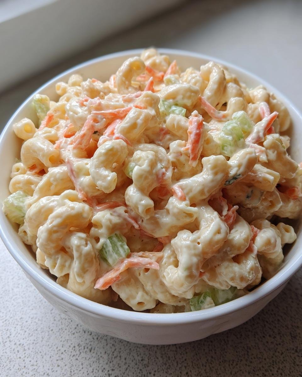 Nahaufnahme von cremiger Hawaiian Macaroni Salad mit Makkaroni, Karottenstreifen und Selleriewürfeln in einer weißen Schüssel.