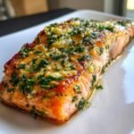 Nahaufnahme von saftigem Knoblauchbutter Gebackenen Lachs auf einem wei&szlig;en Teller.