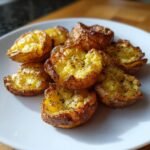 Nahaufnahme von mehreren knusprigen Air Fryer Smashed Potatoes, bestreut mit schwarzem Pfeffer, auf einem wei&szlig;en Teller.