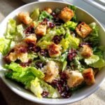 Nahaufnahme einer Sch&uuml;ssel La Scala Chopped Salad mit knackigem Salat, Croutons und getrockneten Cranberries.