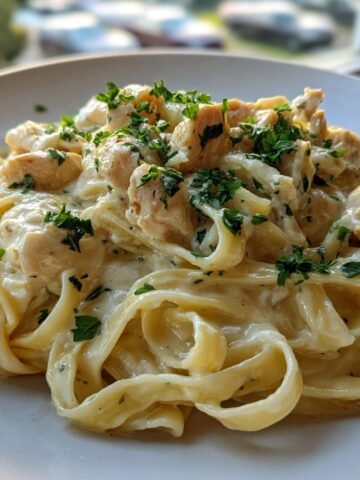 Nahaufnahme von cremigem Lemon Chicken Fettuccine mit Hähnchenstücken und Petersilie garniert.