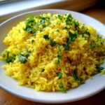 Nahaufnahme von fluffigem, gelbem Lemon Rice, garniert mit frischen gr&uuml;nen Petersilienbl&auml;ttern in einer wei&szlig;en Schale.