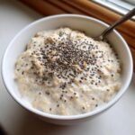 Nahaufnahme von cremigem Protein Oatmeal in einer wei&szlig;en Sch&uuml;ssel, garniert mit Chiasamen.