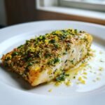 Nahaufnahme von zartem Roasted Mahi Mahi, bedeckt mit Zitronenschale und frischen Kr&auml;utern auf einem wei&szlig;en Teller.