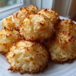 Nahaufnahme von saftigen Kokosmakronen mit goldbraun gebackenen Spitzen auf einem wei&szlig;en Teller.