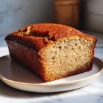 Ein ganzer, frisch gebackener Banana Pound Cake mit goldbrauner Kruste auf einem Teller.