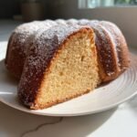 Angeschnittenes St&uuml;ck saftiger Citrus Olive Oil Bundt Cake, best&auml;ubt mit Puderzucker auf einem Teller.
