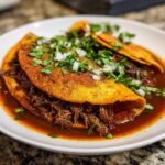 Nahaufnahme von Beef Birria in einer Tortilla, getunkt in reichhaltiger Br&uuml;he und garniert mit Zwiebeln und Koriander.