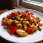 Nahaufnahme von Skinny Cashew Chicken mit roten Paprikast&uuml;cken und Cashewkernen auf einem wei&szlig;en Teller.