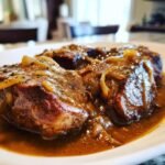 Nahaufnahme von saftigen Smothered Pork Chops, bedeckt mit einer reichhaltigen Zwiebelso&szlig;e.