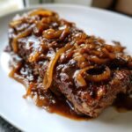 Ein saftiges St&uuml;ck Fleisch bedeckt mit dunkler So&szlig;e und karamellisierten Zwiebelringen, typisch f&uuml;r Onion Gravy Smothered Steak.