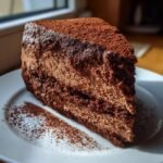 Ein saftiges St&uuml;ck Chocolate Mousse Cake mit mehreren Schichten Mousse auf einem wei&szlig;en Teller, best&auml;ubt mit Kakaopulver.