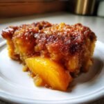 Nahaufnahme eines St&uuml;cks Zimt Zucker Pfirsich Cobbler Dump Cake mit karamellisierter Kruste und saftigem Pfirsich.