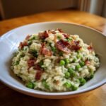 Cremiges Sweet Pea And Crispy Bacon Risotto mit knusprigem Speck garniert in einer wei&szlig;en Sch&uuml;ssel.
