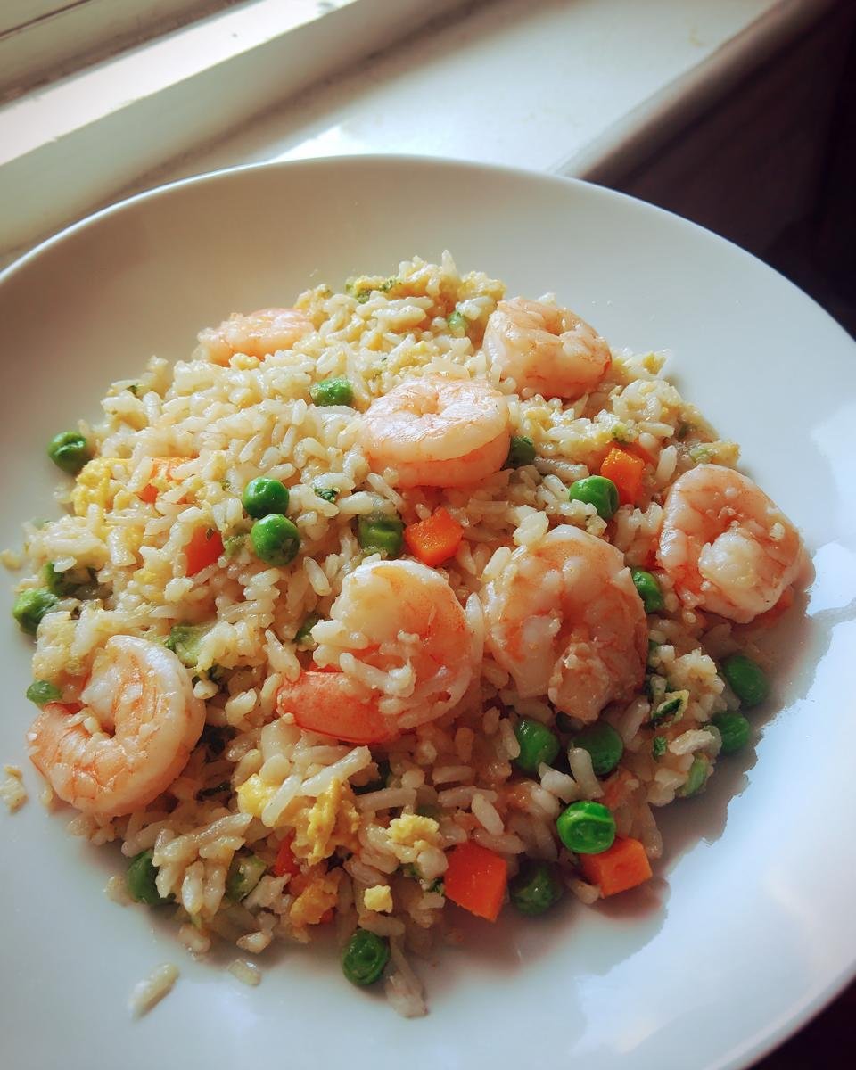Nahaufnahme von k&ouml;stlichem Shrimp Fried Rice mit Garnelen, Erbsen und Karotten auf einem wei&szlig;en Teller.