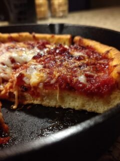 Nahaufnahme einer dicken Scheibe Vollkorn-Deep-Dish-Pfannenpizza mit geschmolzenem Käse und Tomatensauce in einer gusseisernen Pfanne.