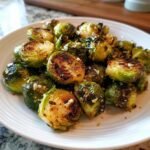 Nahaufnahme von krossen Air Fryer Brussels Sprouts, leicht gebr&auml;unt und mit Gew&uuml;rzen bestreut, auf einem wei&szlig;en Teller.