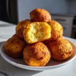 Stapel goldbrauner Air Fryer Hush Puppies, einer davon aufgeschnitten, um die lockere Textur zu zeigen.