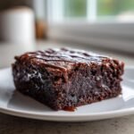 Ein saftiges St&uuml;ck Baileys Irish Cream Brownie mit dunklem Schokoladenguss auf einem wei&szlig;en Teller.