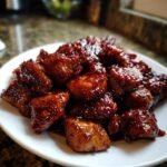 Nahaufnahme von saftigen, glasierten St&uuml;cken Bourbon Chicken auf einem wei&szlig;en Teller.