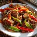 Gebratene St&uuml;cke von Conecuh Sausage mit bunten Paprikastreifen und Zwiebeln auf einem wei&szlig;en Teller.