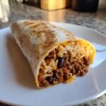 Nahaufnahme eines gef&uuml;llten Burritos mit gew&uuml;rztem Hackfleisch, Reis und schwarzen Bohnen auf einem wei&szlig;en Teller.