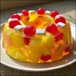 Ein leuchtend gelber Congealed Salad mit Ananasst&uuml;cken, roten Cocktailkirschen und wei&szlig;en Marshmallows.