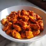 Nahaufnahme von gew&uuml;rfelten, scharf gew&uuml;rzten Chipotle Chicken St&uuml;cken in einer wei&szlig;en Sch&uuml;ssel.