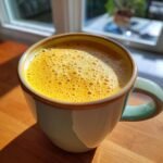 Nahaufnahme eines leuchtend gelben Golden Milk Latte mit feinem Schaum in einer t&uuml;rkisen Tasse.