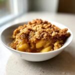 Nahaufnahme von Healthy Apple Cobbler mit goldbrauner Streuseldecke in einer wei&szlig;en Schale.