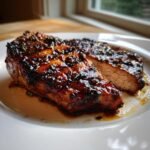 Nahaufnahme eines saftigen Jerk Sauce Grilled Pork Chops mit dunkler, karamellisierter Glasur auf einem wei&szlig;en Teller.