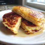 Nahaufnahme von gestapelten Jiffy Cornbread Pancakes, die mit goldbrauner Kruste und Sirup &uuml;bergossen sind.