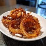 Eine Nahaufnahme von knusprig frittierten Schalottenringen auf einem wei&szlig;en Teller, ideal f&uuml;r Shallot Recipes.