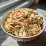 Nahaufnahme von cremigem Krautsalat mit Karottenstreifen in einer wei&szlig;en Sch&uuml;ssel, ideal f&uuml;r Rezepte mit Coleslaw Mix.