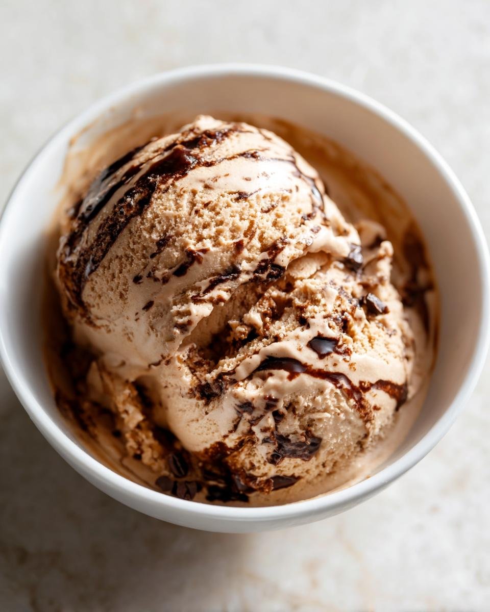 Nahaufnahme von zwei Kugeln Mocha Latte Frozen Yogurt in einer wei&szlig;en Schale, betr&auml;ufelt mit dunkler Schokoladensauce.