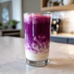 Ein hohes Glas mit einem leuchtend lila und wei&szlig;en geschichteten Smoothie, wahrscheinlich ein Almond Milk Smoothie.