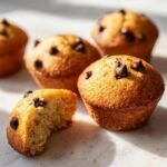 Nahaufnahme von fluffigen Mini Chocolate Chip Muffins auf heller Oberfl&auml;che, einer davon angebissen.