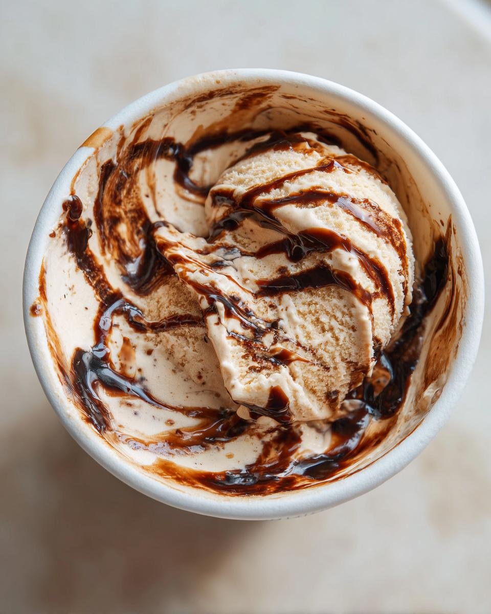 Nahaufnahme von zwei Kugeln Mocha Latte Frozen Yogurt in einer wei&szlig;en Schale, betr&auml;ufelt mit dunkler Schokoladensauce.