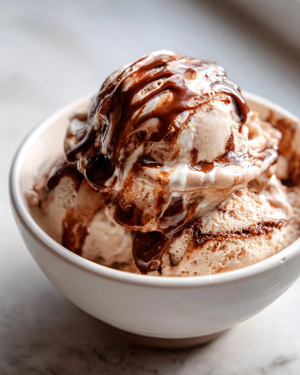 Nahaufnahme von Kugeln Mocha Latte Frozen Yogurt in einer wei&szlig;en Sch&uuml;ssel, &uuml;bergossen mit dunkler Schokoladensauce.