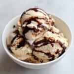 Drei Kugeln Mocha Latte Frozen Yogurt in einer wei&szlig;en Schale, &uuml;bergossen mit dunkler Schokoladensauce.