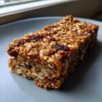 Nahaufnahme eines selbstgemachten M&uuml;sliriegel mit Haferflocken und getrockneten Fr&uuml;chten auf einem grauen Teller.