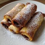 Nahaufnahme von vier Nutella French Toast Rollups, goldbraun gebraten und mit Puderzucker best&auml;ubt.