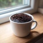 Nahaufnahme eines fertigen Oreo Mug Cake mit dunkler, kr&uuml;meliger Oberfl&auml;che in einer wei&szlig;en Tasse.