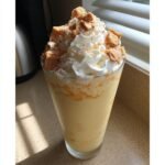 Ein cremiger Peach Cobbler Milkshake in einem Glas, gekr&ouml;nt mit viel Schlagsahne und Keksst&uuml;cken.