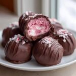 Nahaufnahme von Peppermint Raspberry Chocolate Oreo Balls, einer angeschnitten, die rosa F&uuml;llung zeigt.