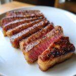 Aufgeschnittenes, medium-rare Wagyu Beef Steak mit knuspriger Kruste auf einem wei&szlig;en Teller.