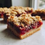 Nahaufnahme eines St&uuml;cks Pomegranate Apple Pie Bars mit saftiger roter F&uuml;llung und knusprigen Streuseln.