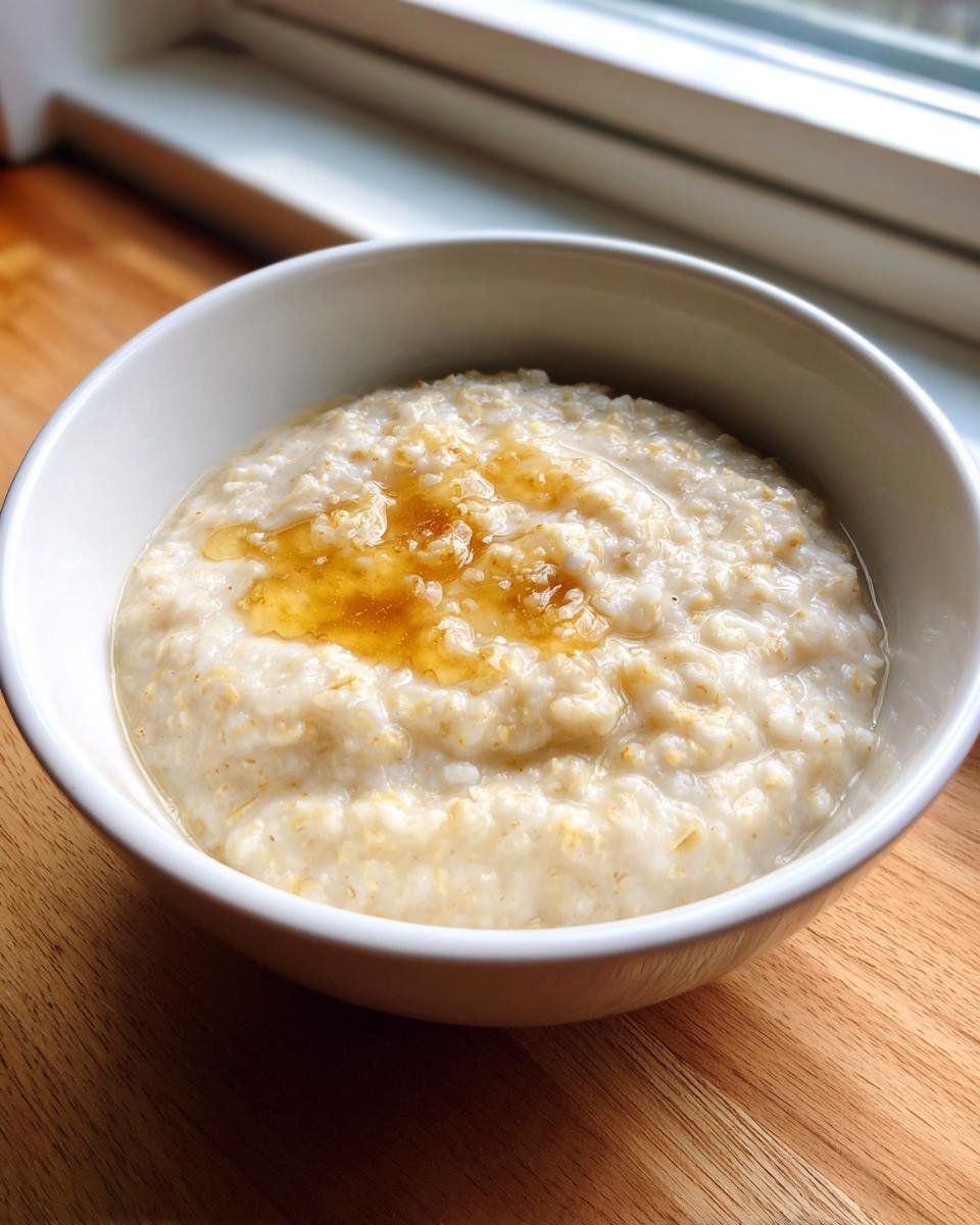 Eine wei&szlig;e Sch&uuml;ssel mit cremigem Porridge, betr&auml;ufelt mit goldbraunem Honig, als Beispiel f&uuml;r Porridge Recipes.