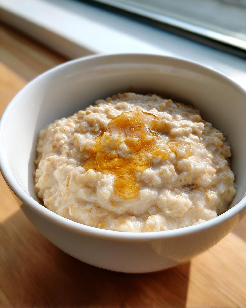Nahaufnahme von cremigem Porridge in einer wei&szlig;en Schale, betr&auml;ufelt mit goldgelbem Honig. Perfekt f&uuml;r Porridge Recipes.