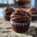 Nahaufnahme eines saftigen Spooky Double Chocolate Cupcakes mit dunkler Schokoladencreme.